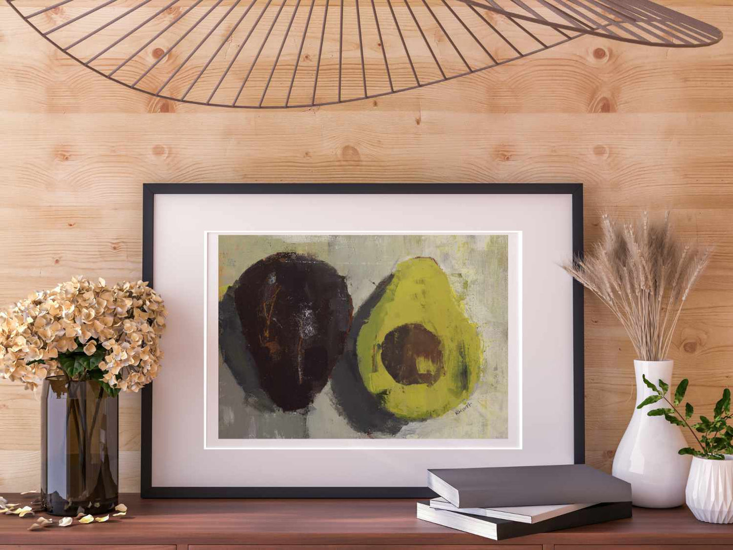 Avocado fine art print shown in black frame with wooden panelling behind and brown flowers